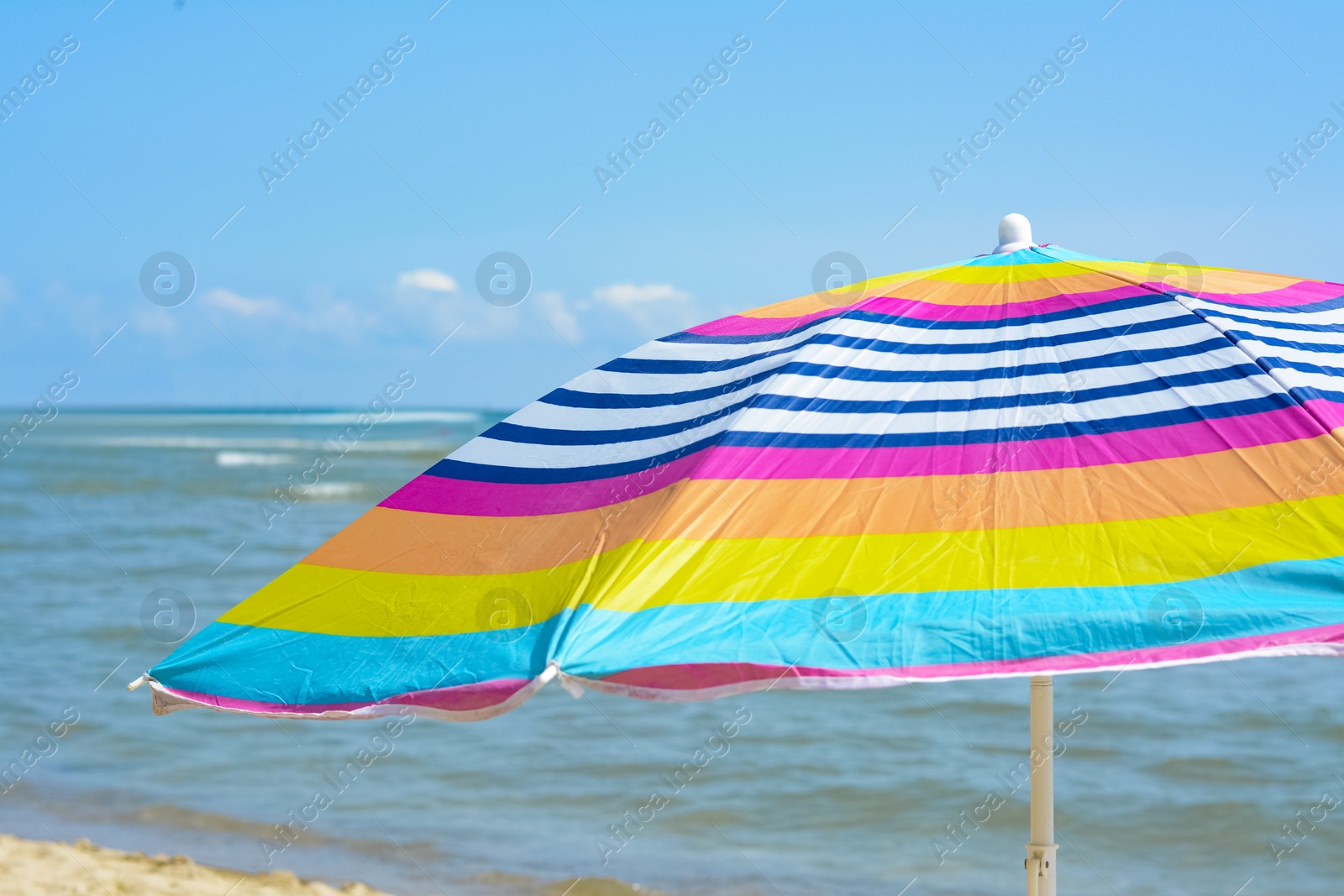 Photo of Colorful striped beach umbrella near sea sunny day, closeup