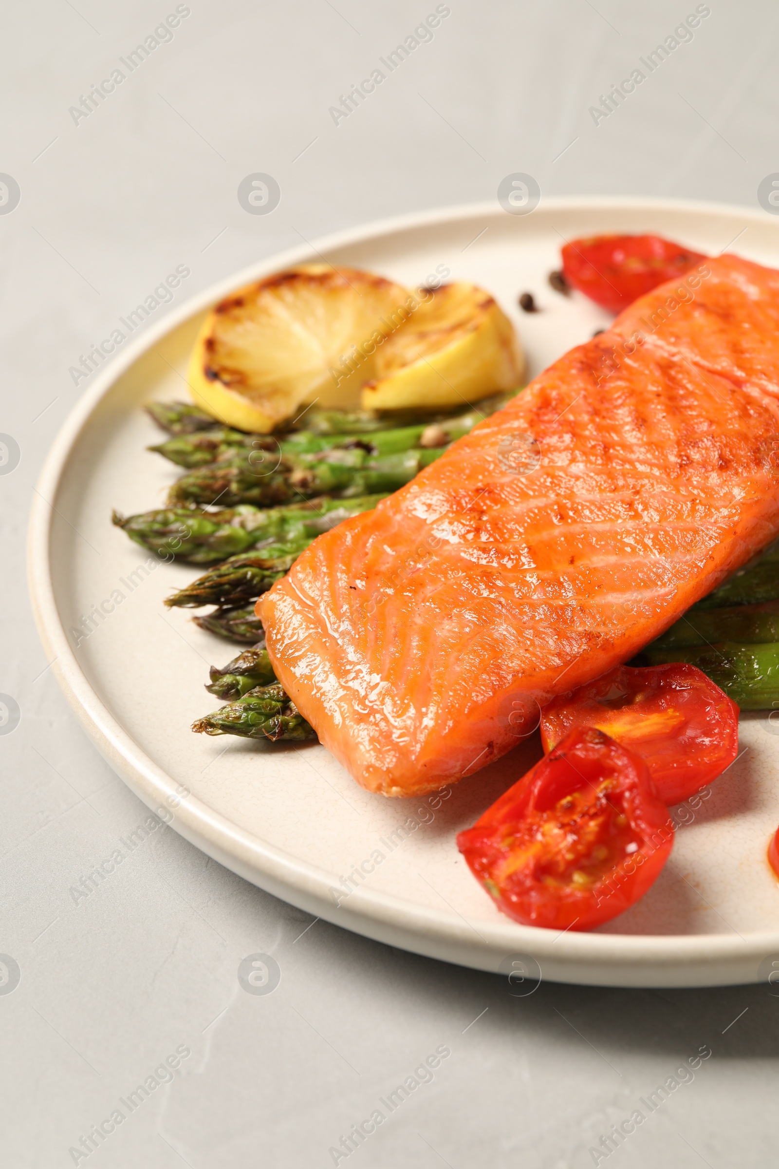 Photo of Tasty grilled salmon with asparagus, tomatoes, spices and lemon on light grey table, closeup