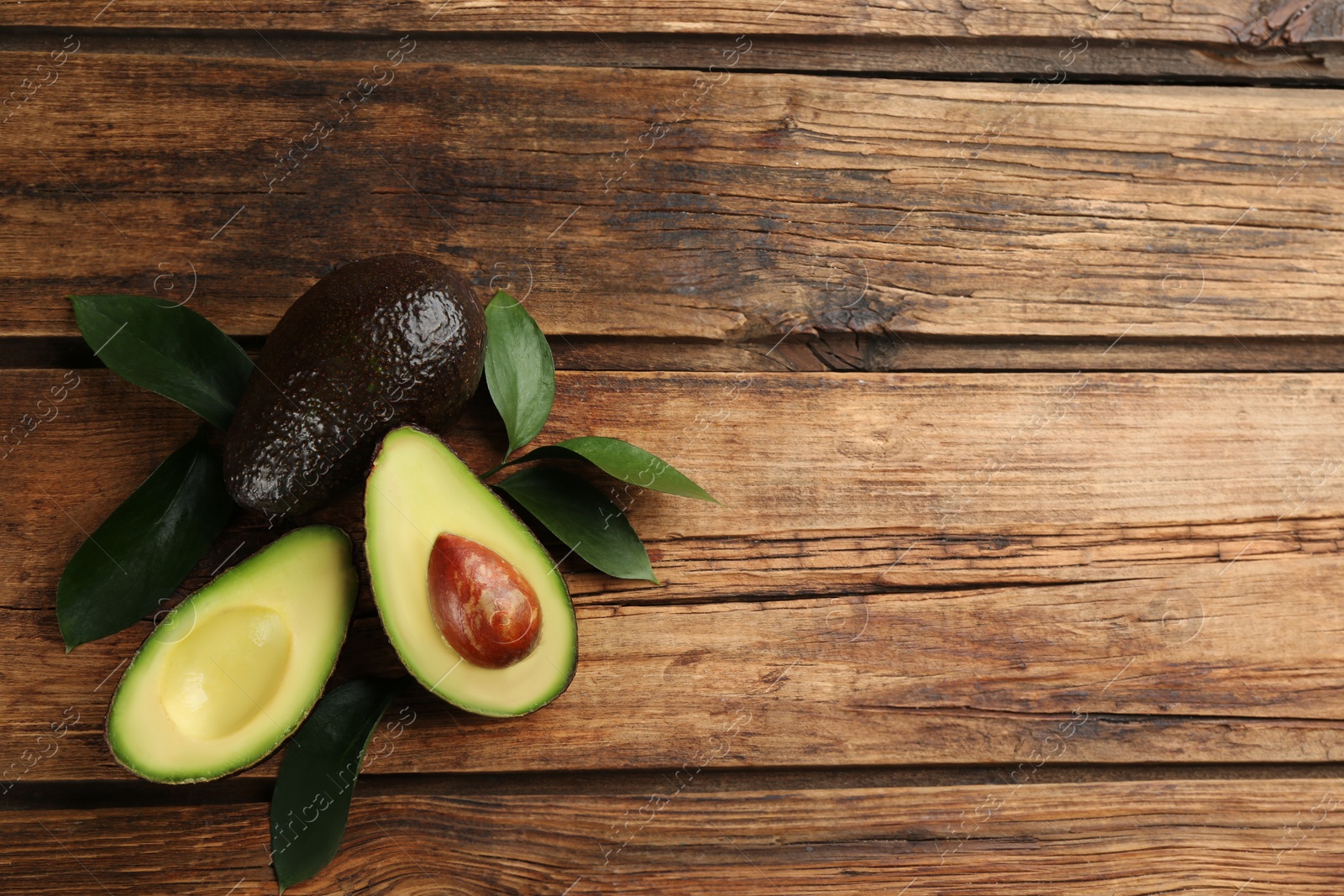 Photo of Whole and cut avocados with green leaves on wooden table, flat lay. Space for text