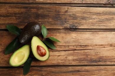 Whole and cut avocados with green leaves on wooden table, flat lay. Space for text