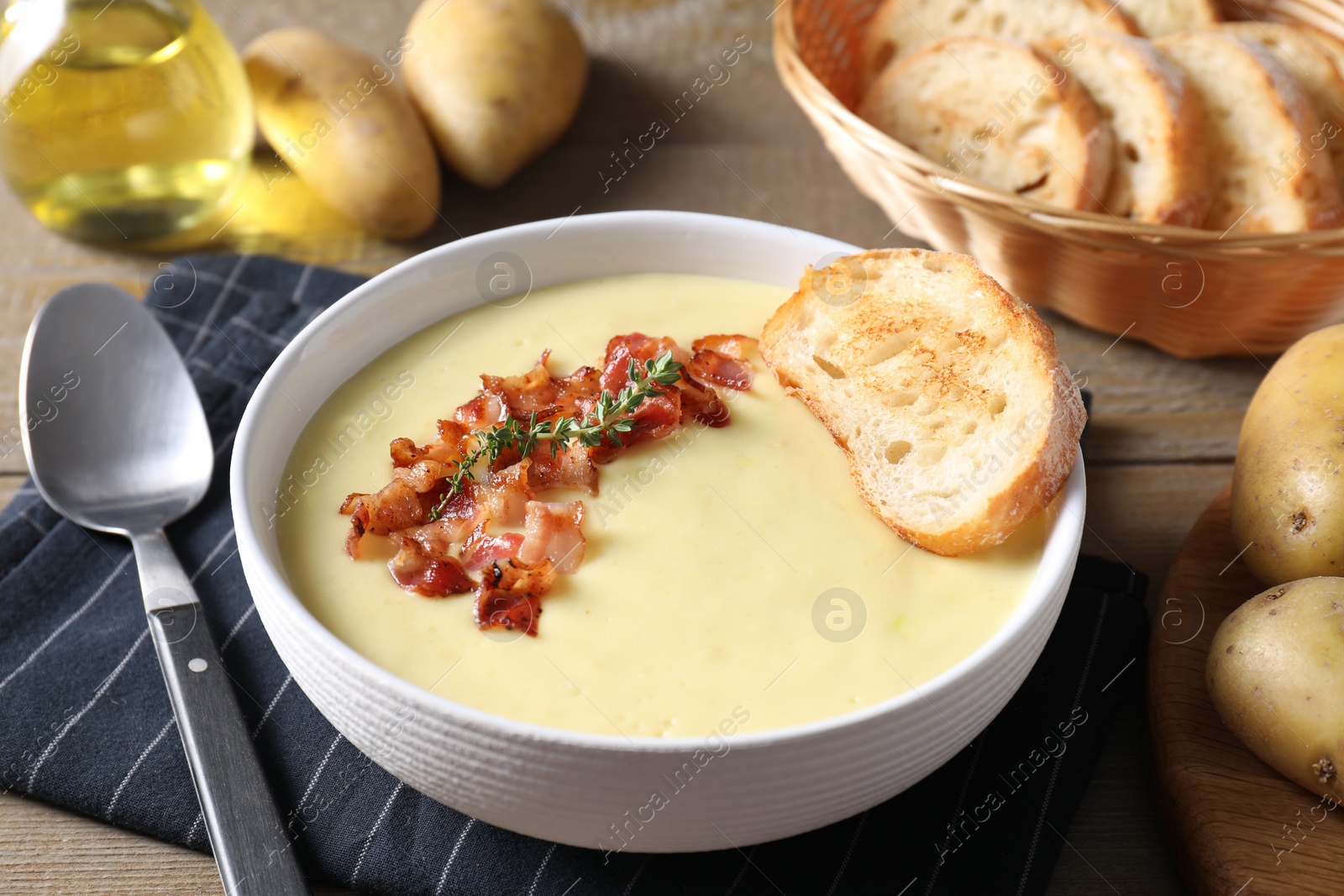 Photo of Tasty potato soup with bacon and rosemary in bowl served on wooden table