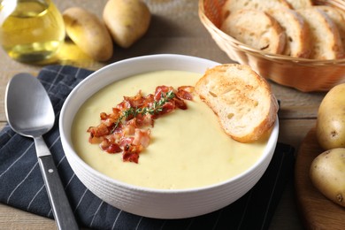 Photo of Tasty potato soup with bacon and rosemary in bowl served on wooden table