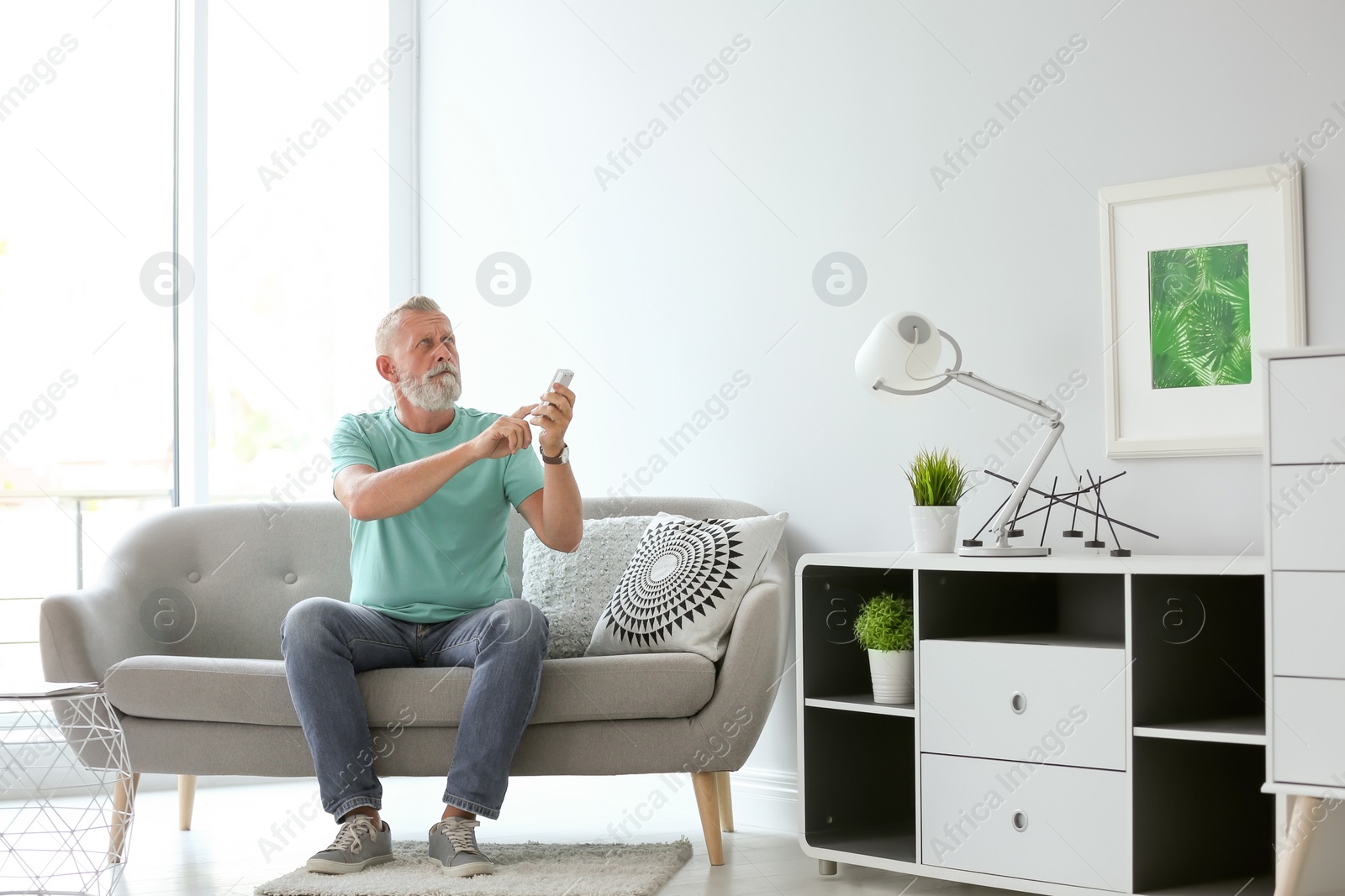 Photo of Senior man with air conditioner remote control at home