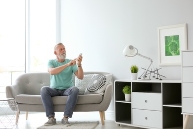 Photo of Senior man with air conditioner remote control at home
