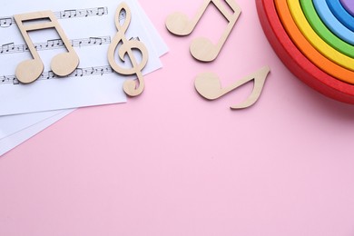 Photo of Baby songs. Music sheets, wooden notes and toy rainbow on pink background, flat lay with space for text