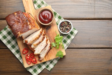 Pieces of baked pork belly served with sauce, chili pepper and parsley on wooden table, top view. Space for text