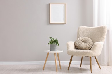 Photo of Comfortable armchair, side table and houseplant near light grey wall indoors. Space for text