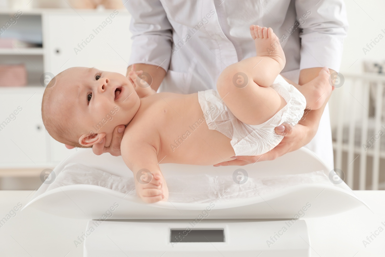 Photo of Doctor weighting baby on scales in light room