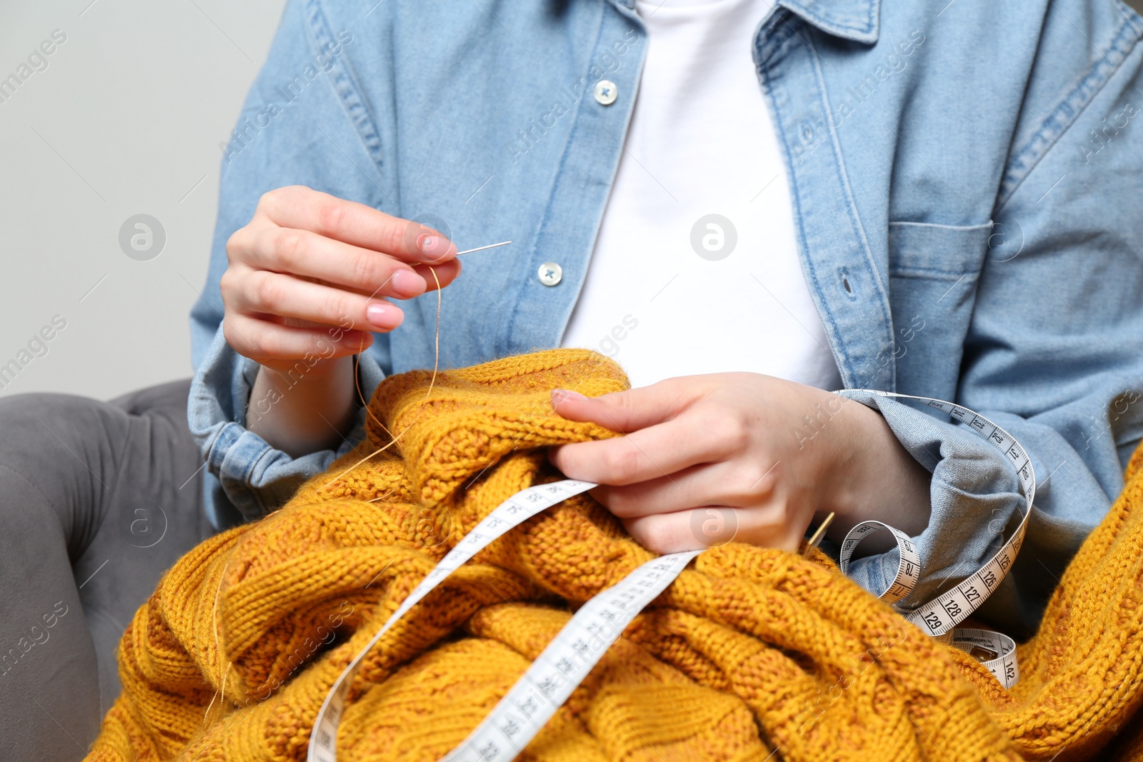 Photo of Woman sewing sweater with needle at home, closeup