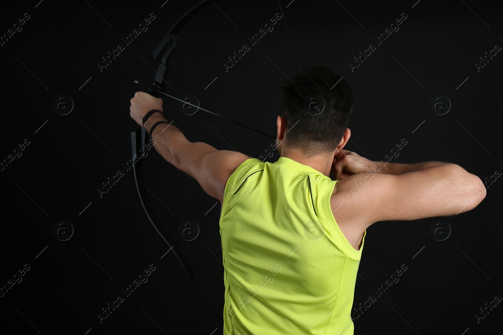 Photo of Man with bow and arrow practicing archery on black background, back view