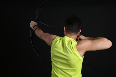 Man with bow and arrow practicing archery on black background, back view