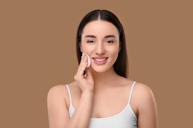 Photo of Beautiful woman removing makeup with cotton pad on beige background