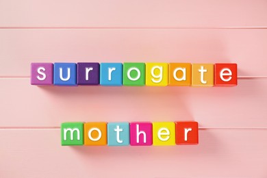 Colorful cubes with words Surrogate Mother on pink wooden table, flat lay