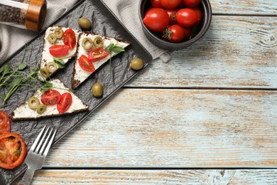 Delicious ricotta bruschettas with fresh tomatoes, olives and greens on wooden table, flat lay. Space for text