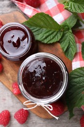 Photo of Delicious raspberry jam, fresh berries and green leaves on wooden table, flat lay