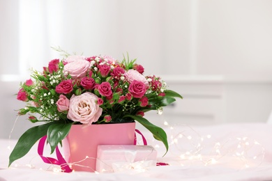 Beautiful bouquet of flowers with gift box and fairy lights on blurred background