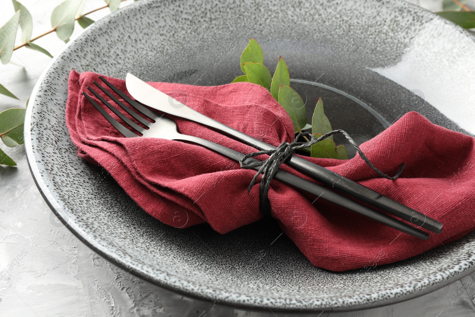 Photo of Stylish setting with cutlery, napkin, eucalyptus branches and plate on grey textured table, closeup