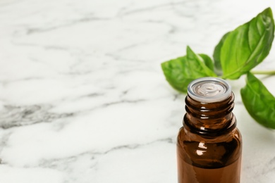 Photo of Bottle of basil essential oil and fresh leaves on marble table. Space for text