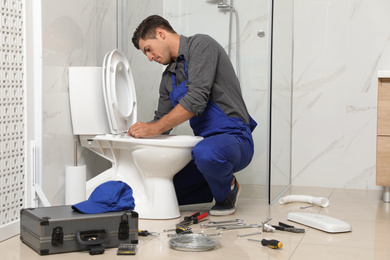 Professional plumber working with toilet bowl in bathroom