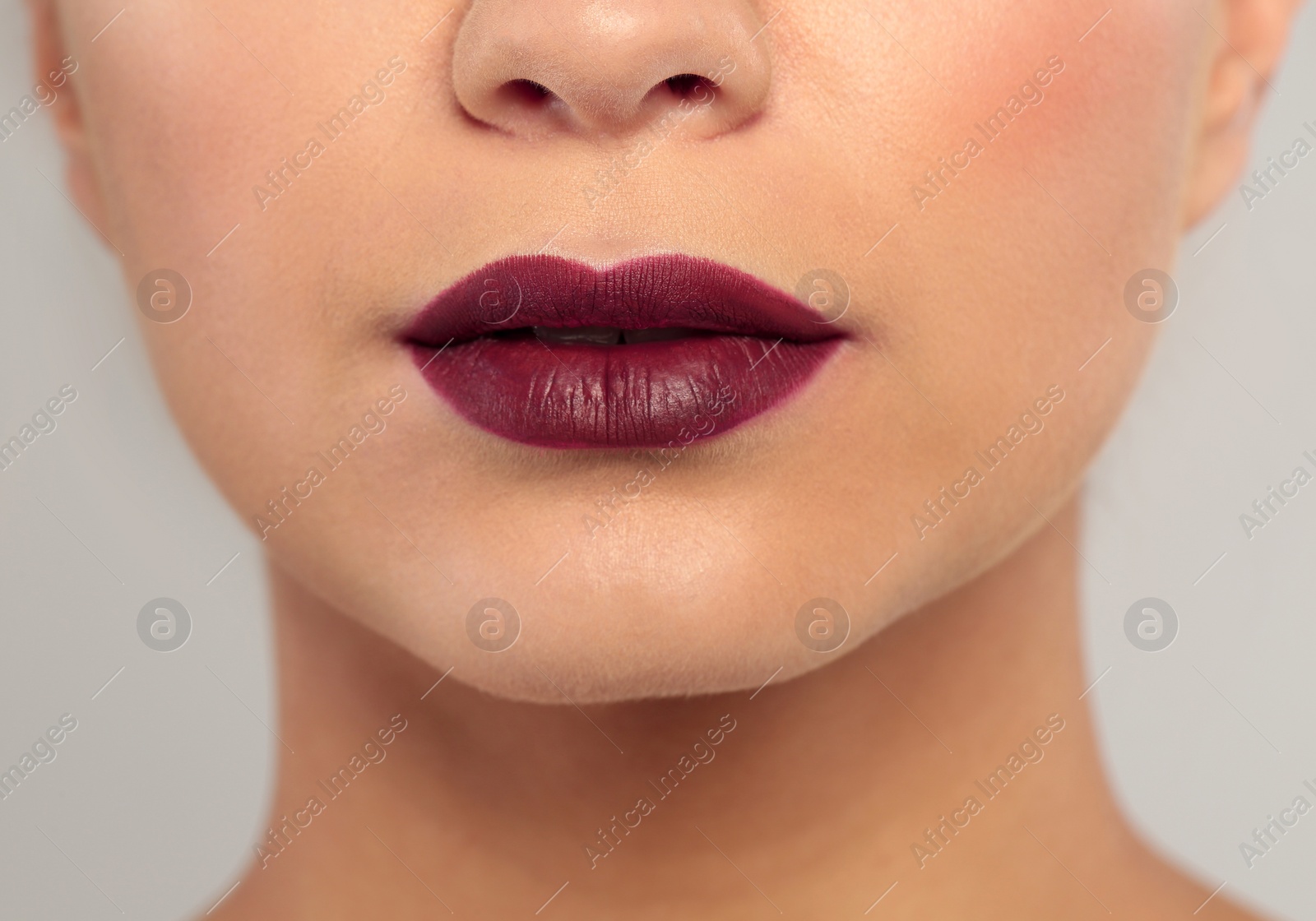Photo of Young woman wearing dark lipstick on gray background, closeup