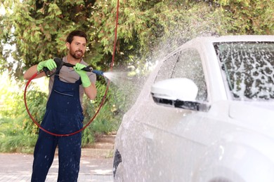 Worker washing auto with high pressure water jet at outdoor car wash