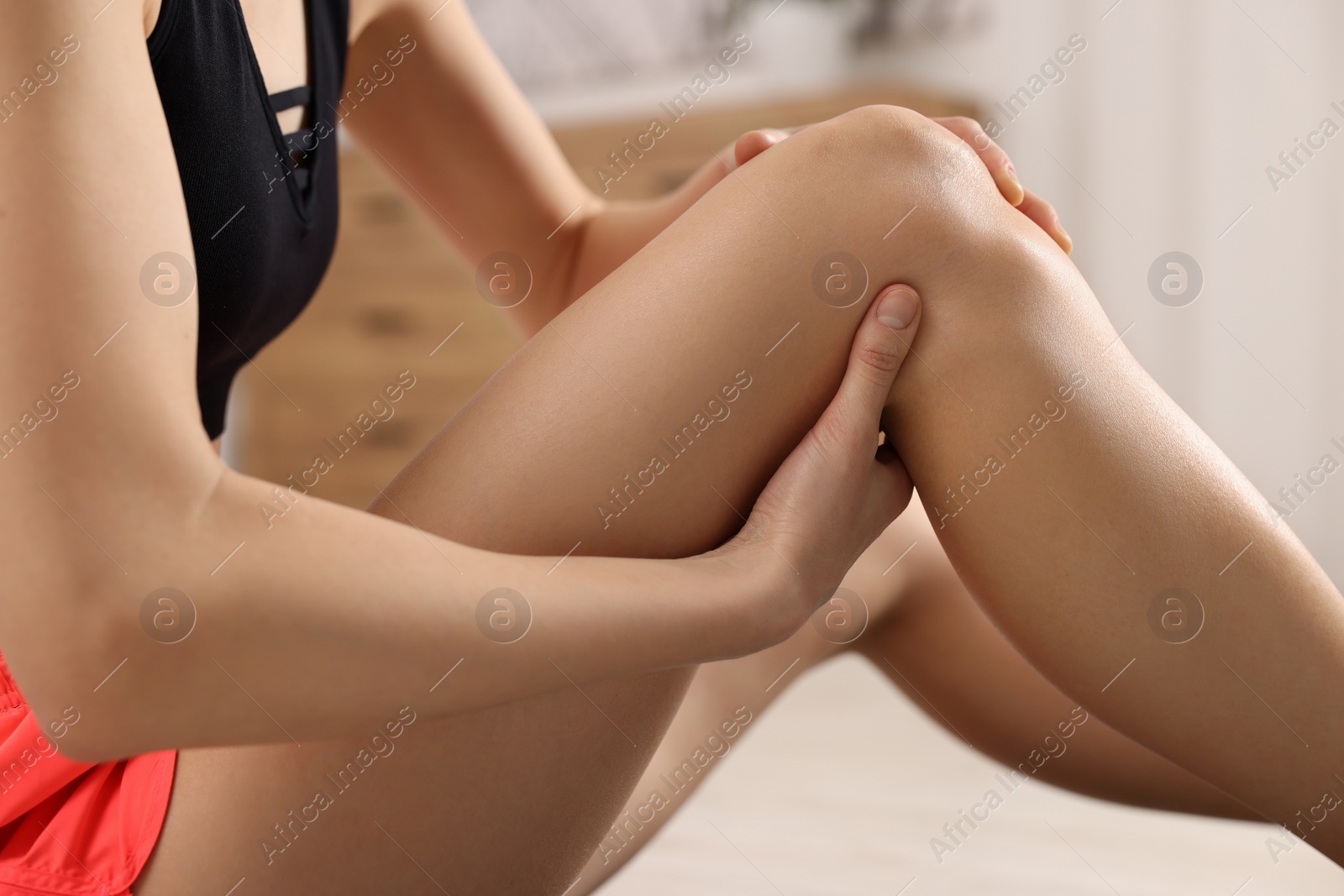 Photo of Woman suffering from leg pain in room, closeup