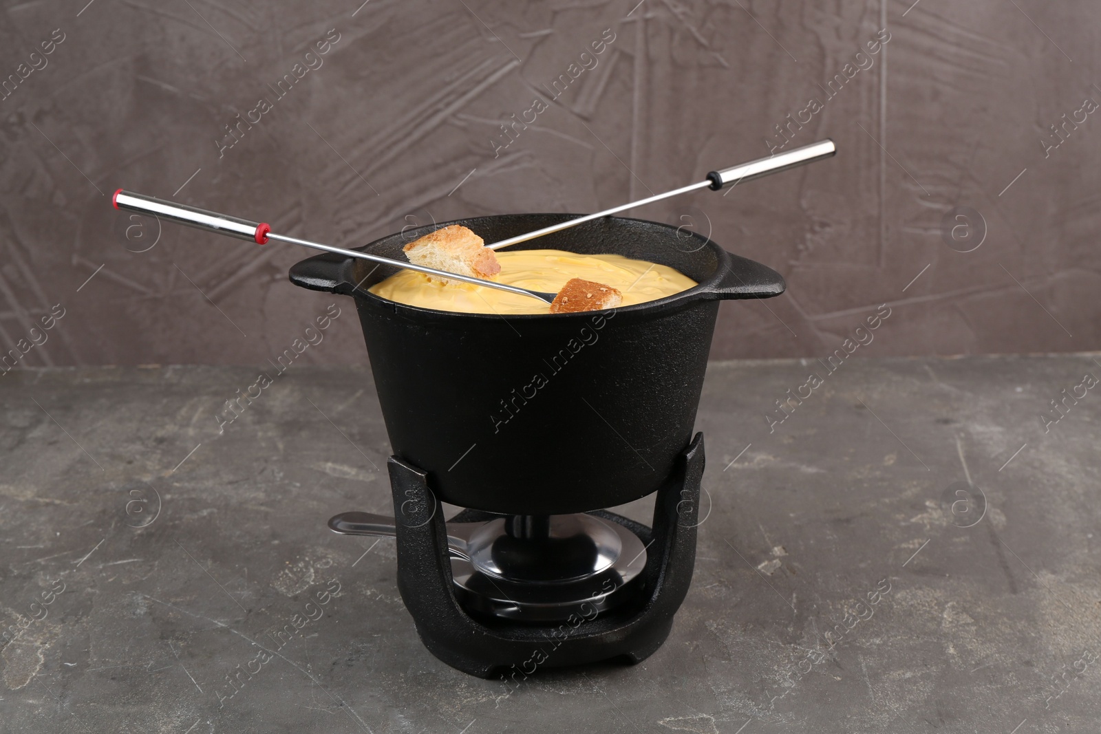 Photo of Fondue pot with tasty melted cheese, forks and bread on grey table