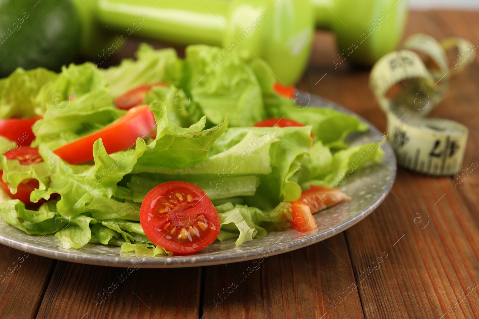 Photo of Healthy diet. Salad, dumbbells and measuring tape on wooden table, closeup