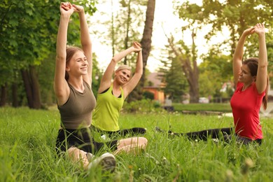 Women and teenage girl doing morning exercise on green grass in park