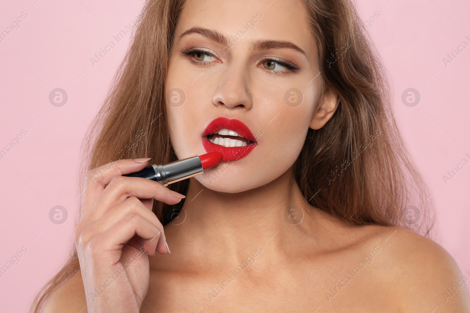 Photo of Young woman applying red lipstick on color background