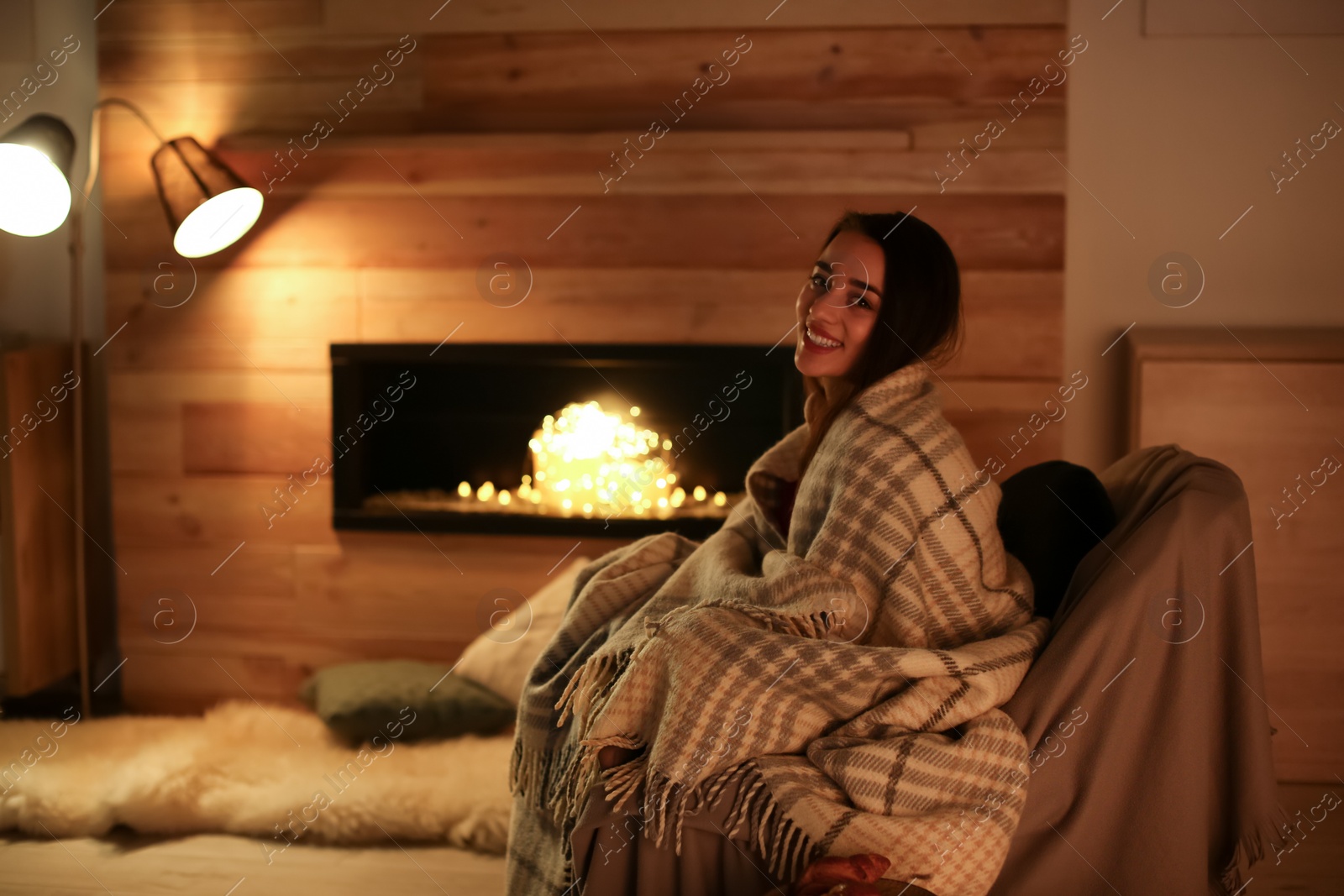 Photo of Young woman resting near decorative fireplace at home. Winter season