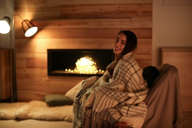 Young woman resting near decorative fireplace at home. Winter season