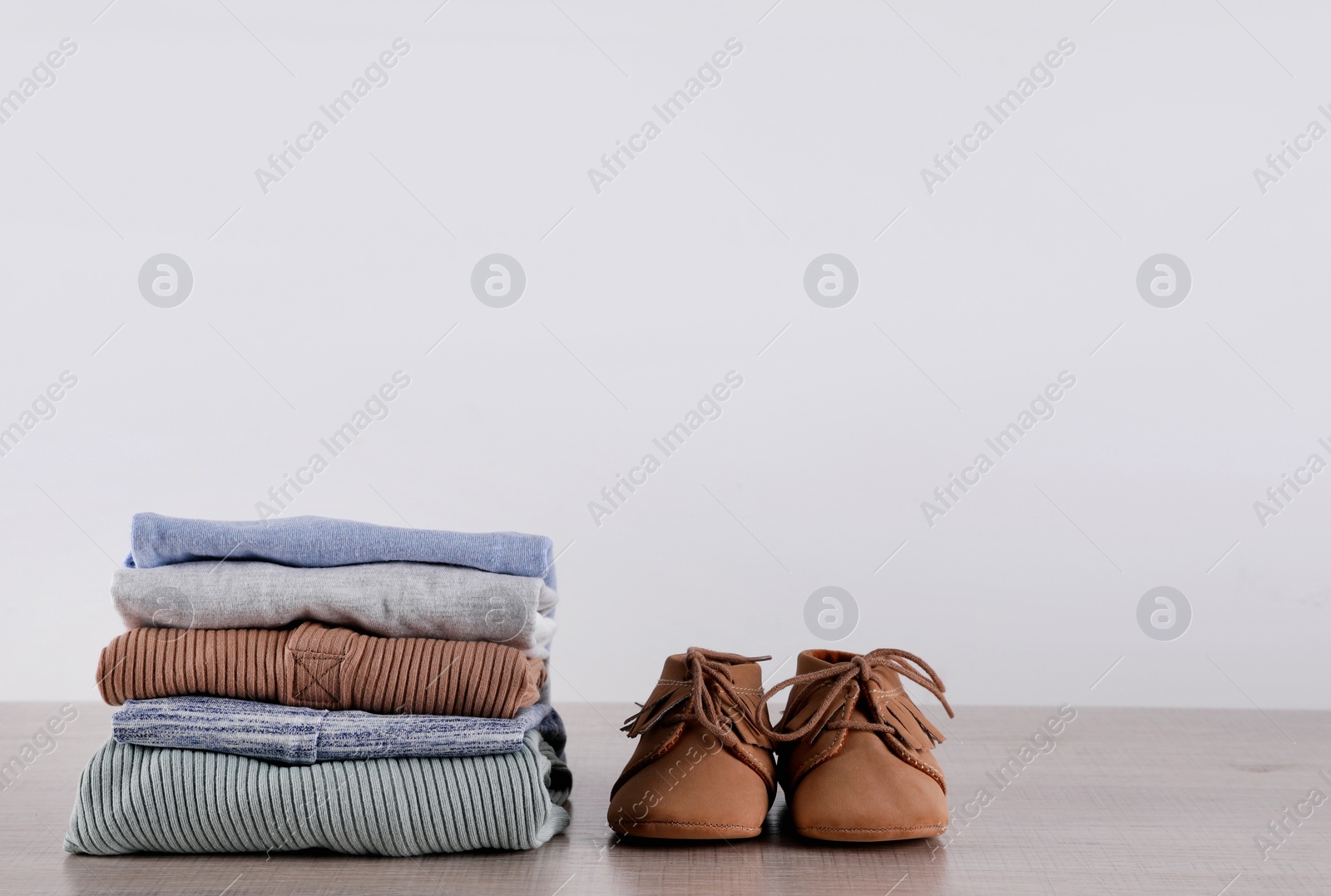 Photo of Stack of baby boy's clothes and shoes on wooden table against white background, space for text