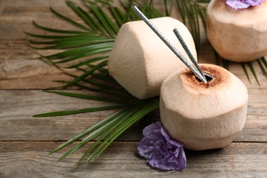 Photo of Fresh coconuts with drinking straws and flower on wooden table. Space for text