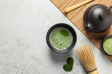 Cup of fresh matcha tea, bamboo whisk, teapot, spoon and green powder on light grey table, top view. Space for text