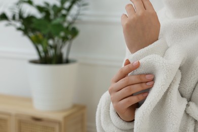 Photo of Woman touching sweater made of soft white fabric indoors, closeup