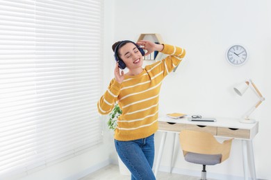Photo of Happy woman in headphones listening music and dancing in cosy room