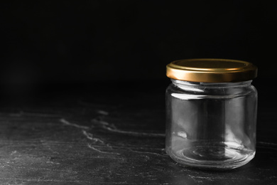 Photo of Empty glass jar on black stone table, space for text