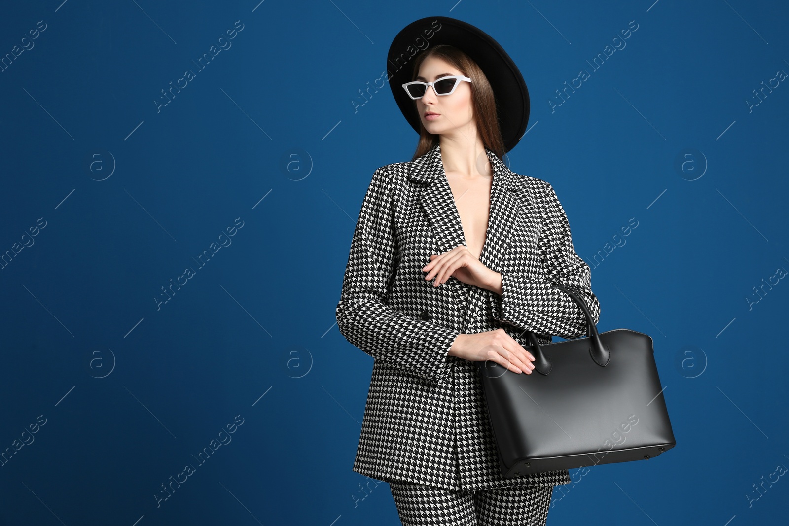 Photo of Beautiful young woman in sunglasses with stylish bag on blue background. Space for text