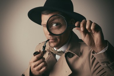 Male detective with smoking pipe looking through magnifying glass on beige background