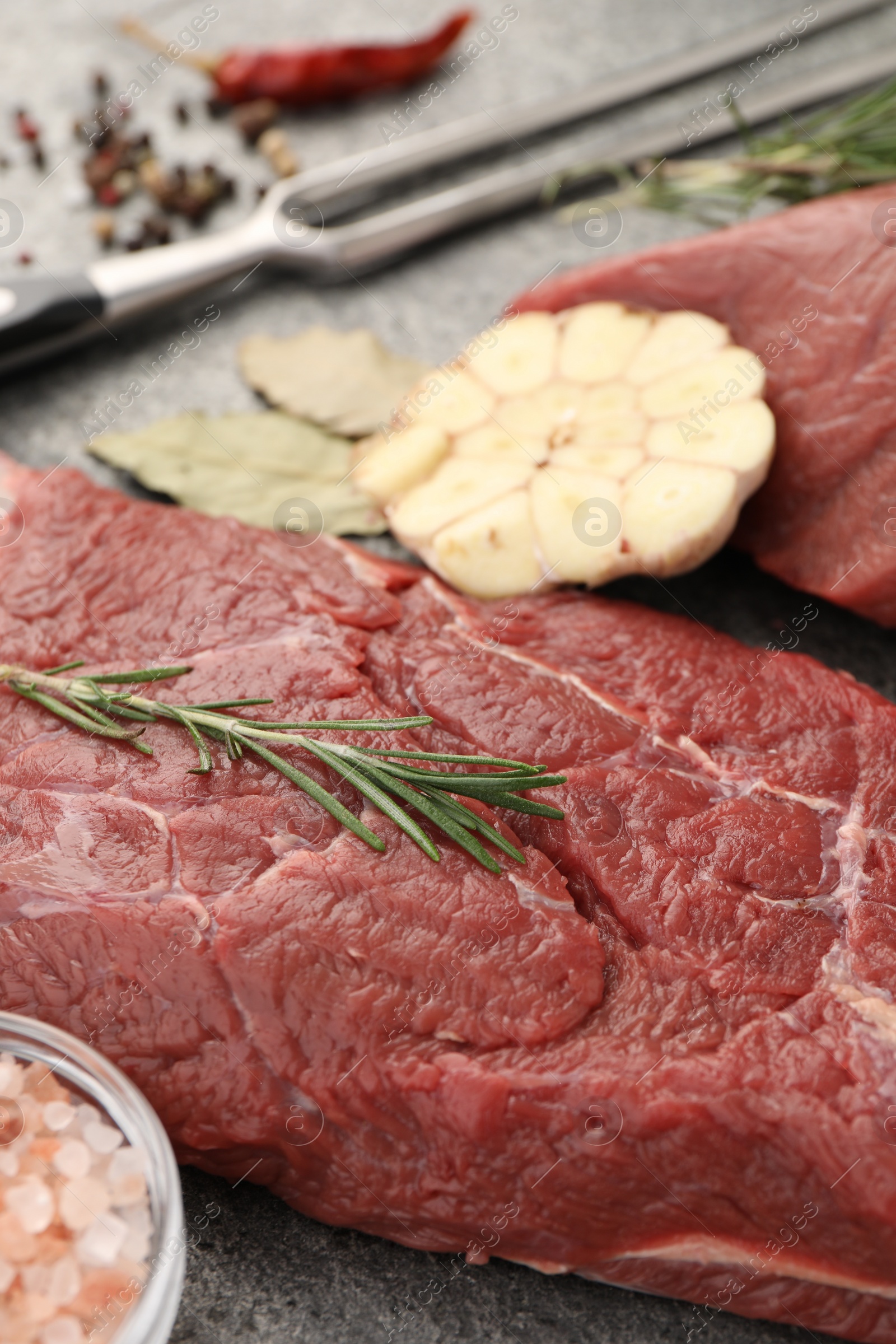 Photo of Piece of raw beef meat with spices and rosemary on table, closeup