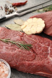 Piece of raw beef meat with spices and rosemary on table, closeup