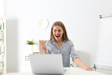 Emotional young woman with laptop celebrating victory in office