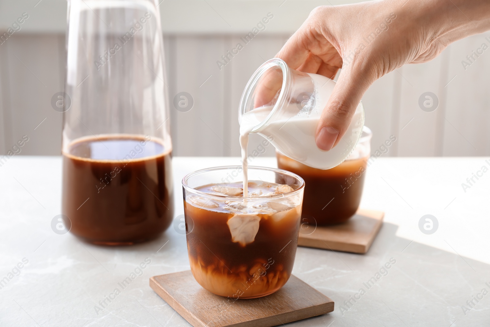 Photo of Woman pouring milk into glass with cold brew coffee on table