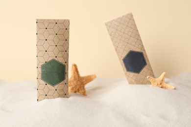 Photo of Scented sachets and starfishes in sand against beige background