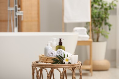 Spa products, burning candles, plumeria flower and tropical leaf on table in bathroom