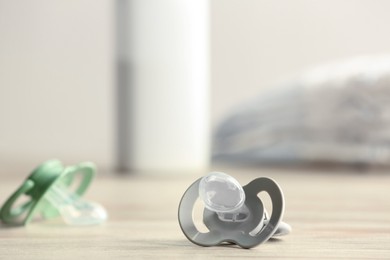 Photo of Baby pacifiers on beige table against blurred background, space for text