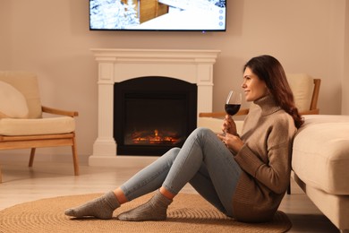 Photo of Young woman with glass of wine relaxing on floor near fireplace at home