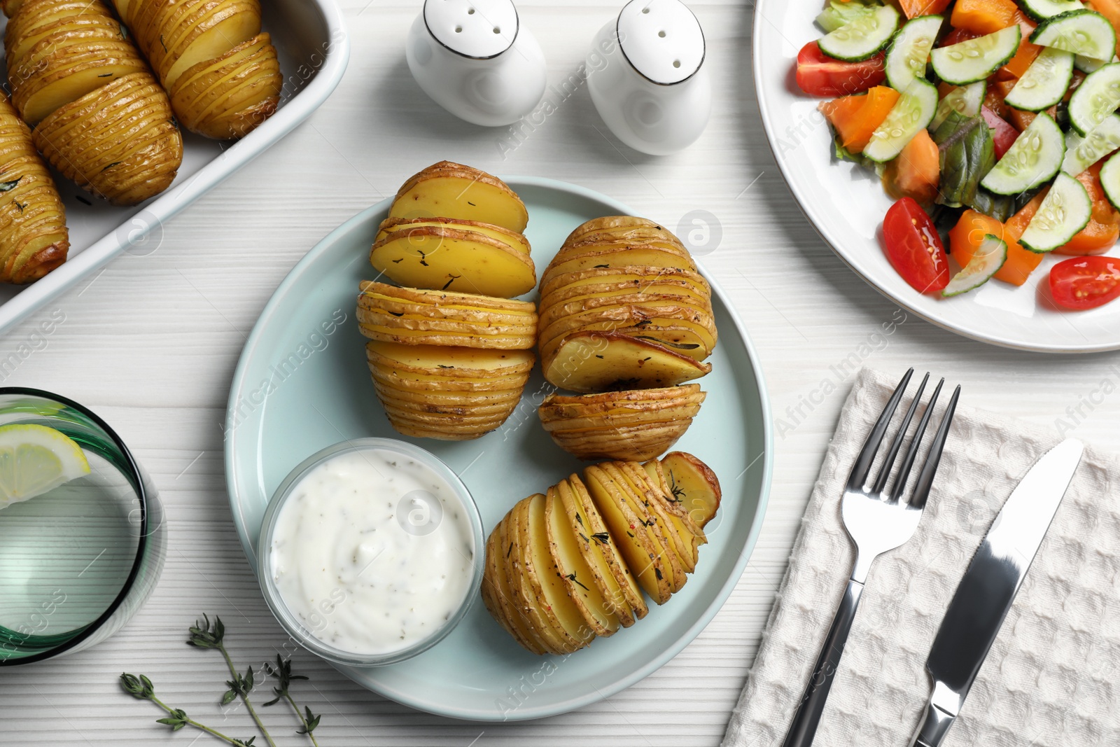 Photo of Delicious homemade Hasselback potatoes served on white wooden table, flat lay