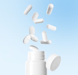 Image of Many different white pills falling into bottle on light blue background